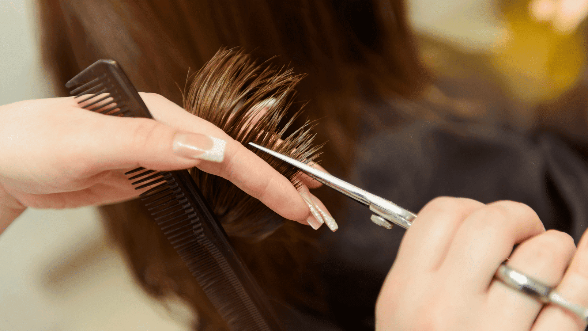Haircut in progress with scissors and comb on brown hair close-up.