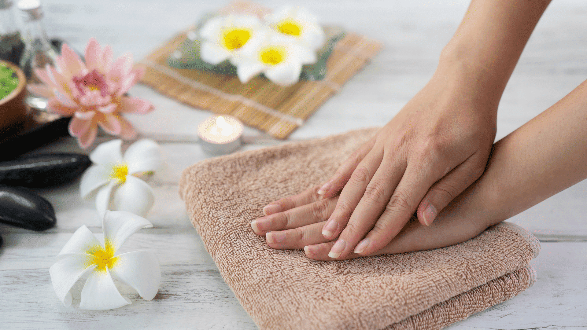 Hands pressing on towel near spa flowers and stones, creating a relaxing atmosphere.