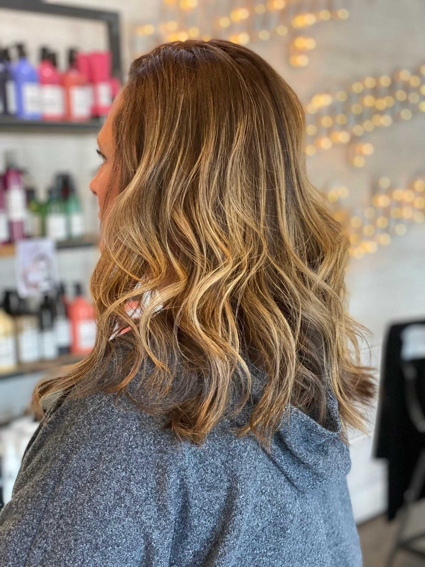 Woman with wavy blonde hair in salon, shelves with hair products in background.