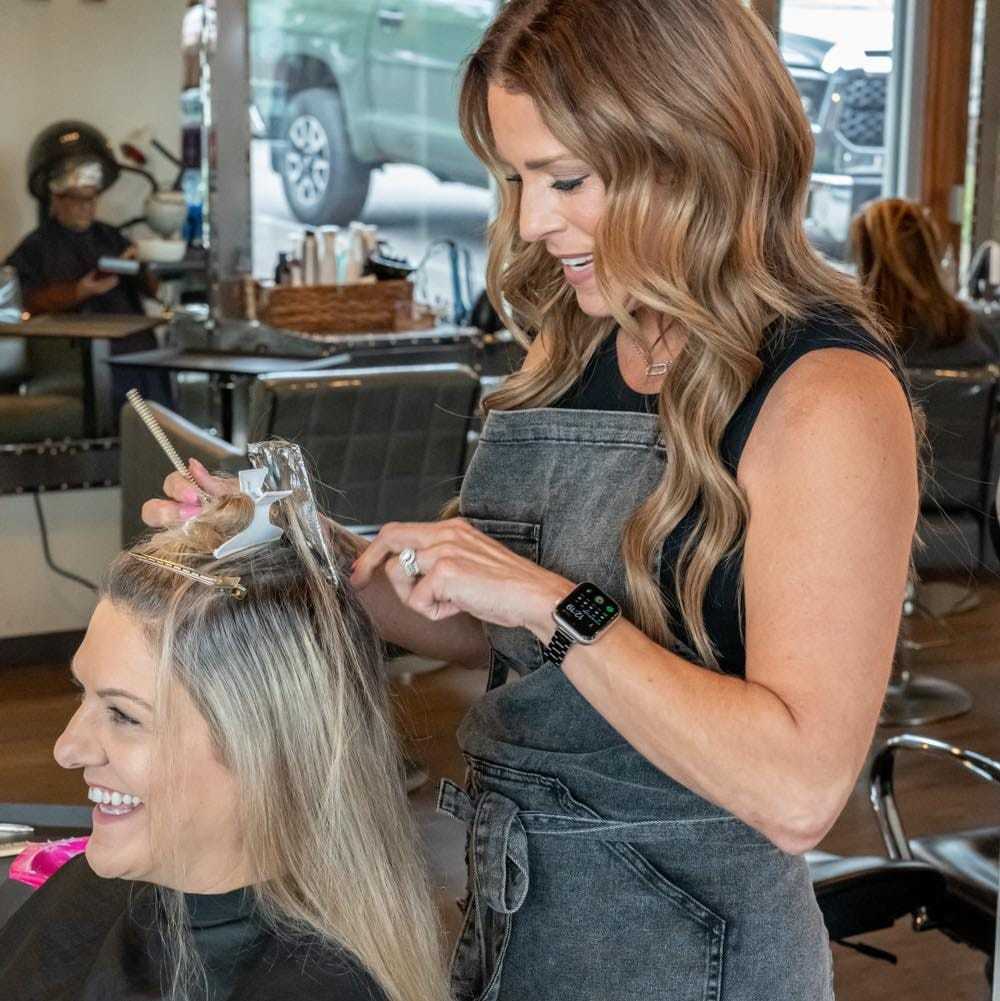 Hair stylist applying highlights to a client's hair in a salon.