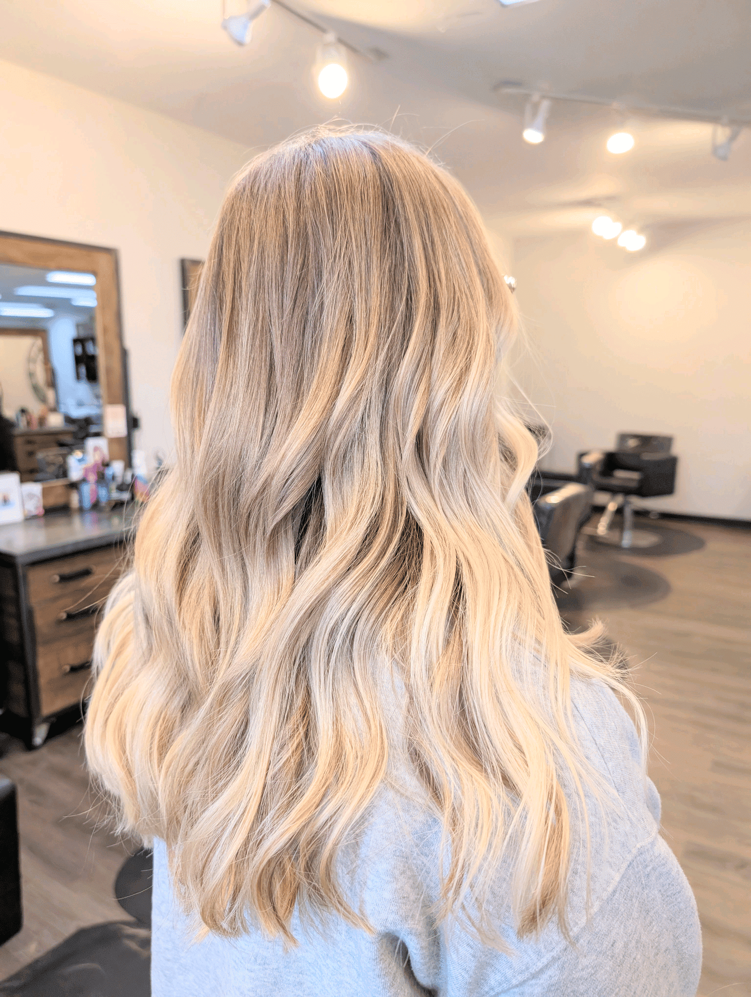 Blonde-haired person in a salon with wavy hair, facing away from the camera.