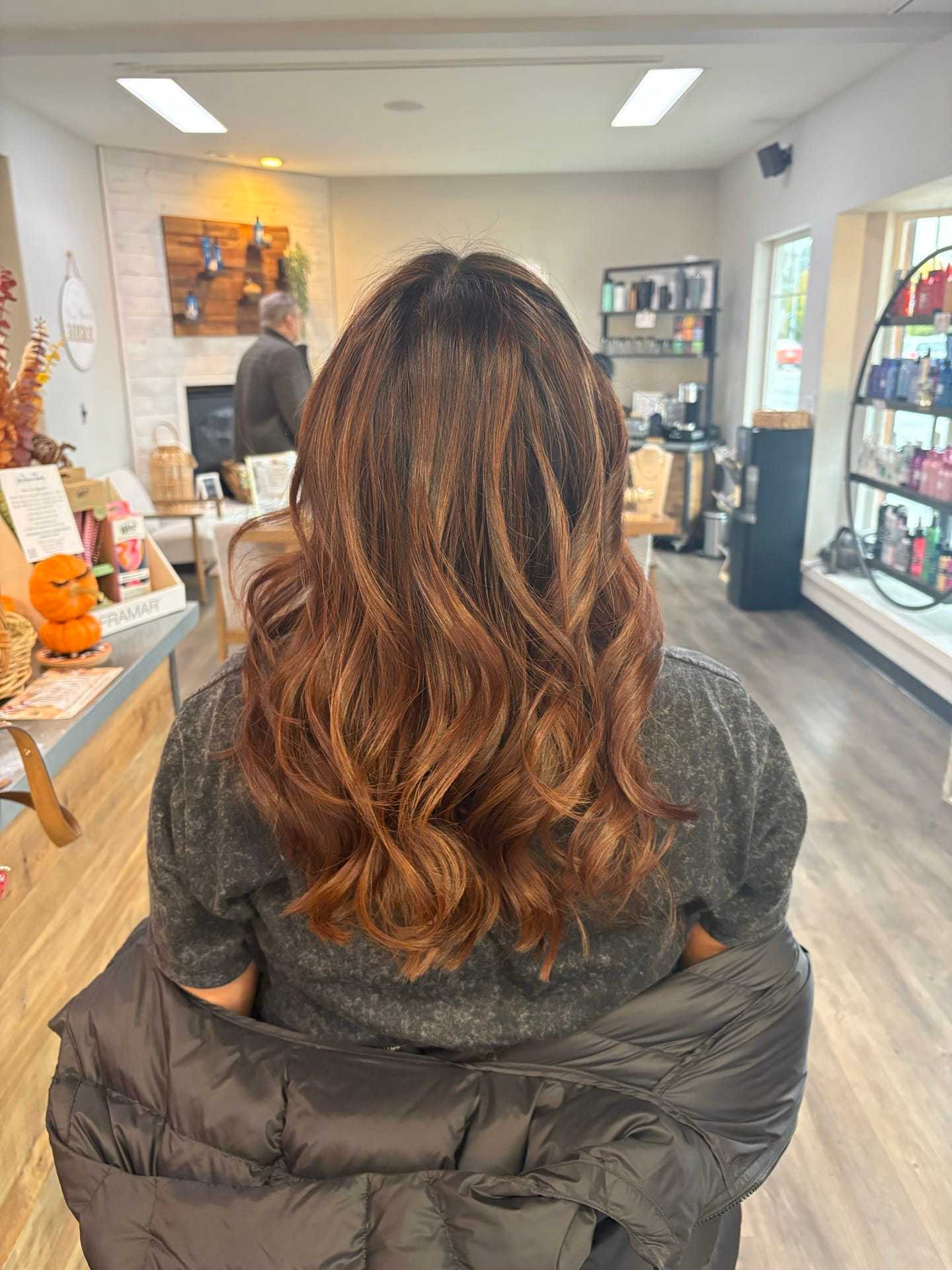 Wavy auburn hair styled at a salon, jacket over shoulders, cozy atmosphere.