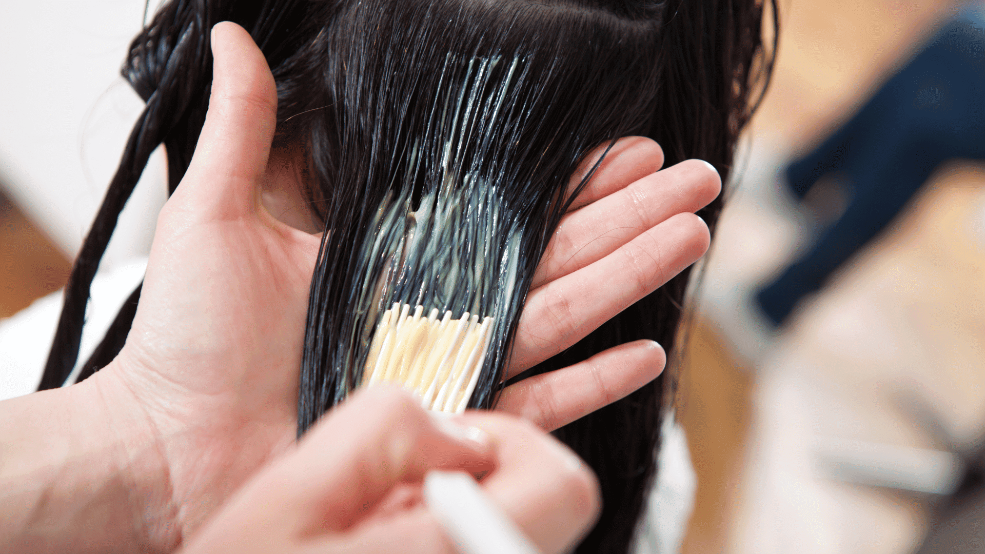 Hairdresser applying conditioner to a client's wet hair in a salon.