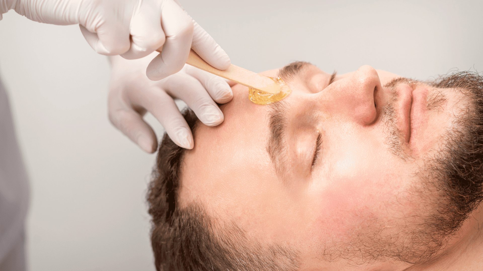 Man receiving facial waxing with applicator on forehead.